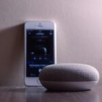 A modern smart speaker and smartphone on a wooden table, indoors.