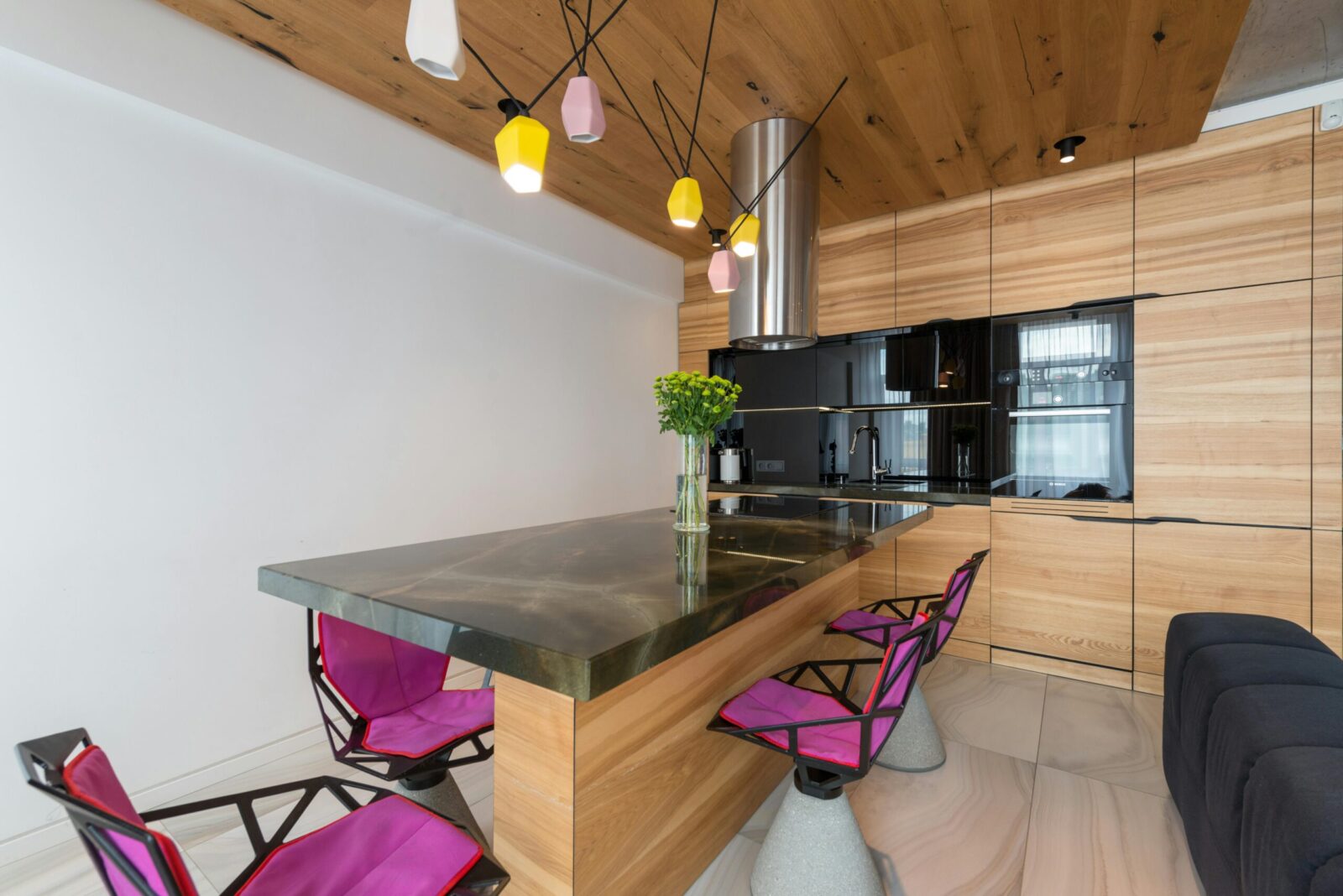 Stylish interior of contemporary kitchen with built in microwave and oven with stylish chairs around marble counter